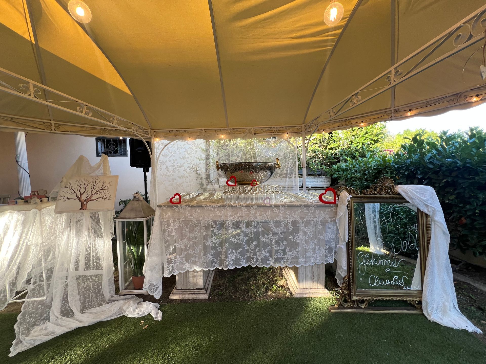 Tavolo del ricevimento nuziale con decorazioni sotto una tenda: pizzo bianco, specchio e cuori rossi.