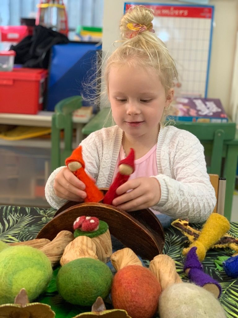 Toddler climbing red ladder on a playground, wearing denim overalls, looking up.