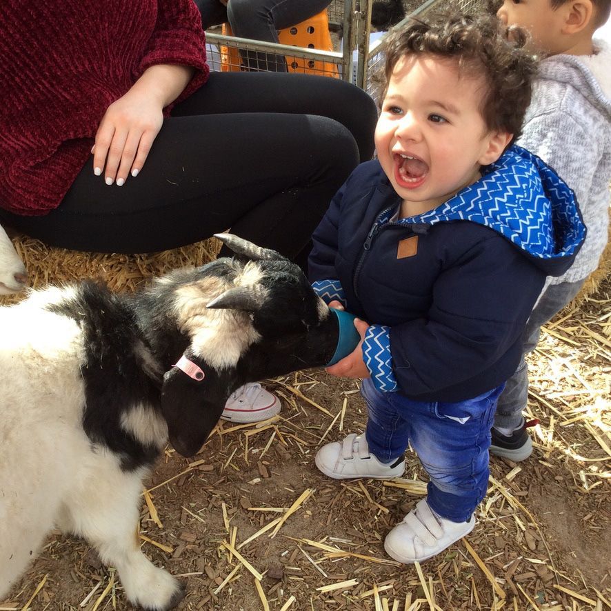 Child holding a colorful beaded toy up, looking up with open mouth, in a classroom setting.