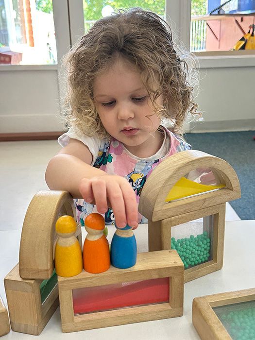 Girl with a pink hair bow focused on a colorful toy with pegs and holes at a table.