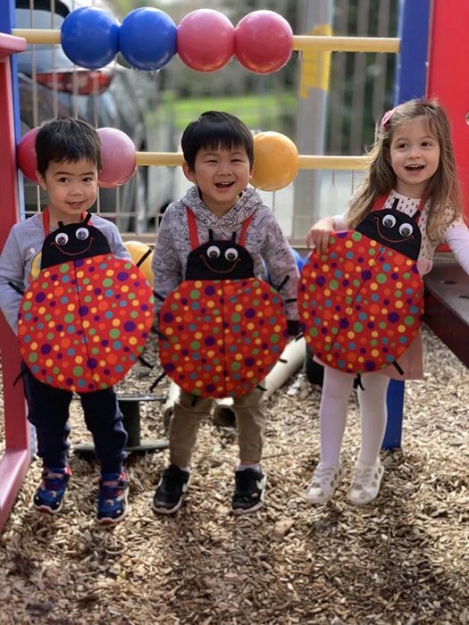 Two children playing with water in a green bin, using a blue watering can to pour water onto a yellow toy.