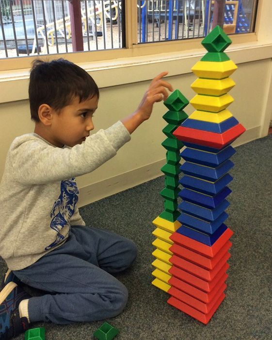 Child building with colorful wooden blocks. Indoors, focused expression.
