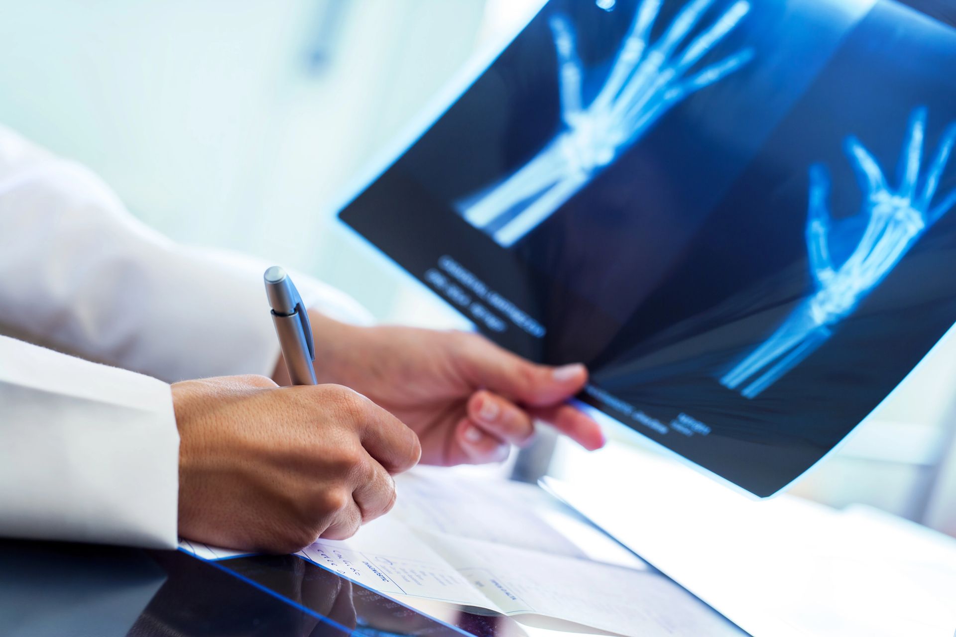 Un médico está mirando una radiografía de una mano y escribiendo en un trozo de papel.