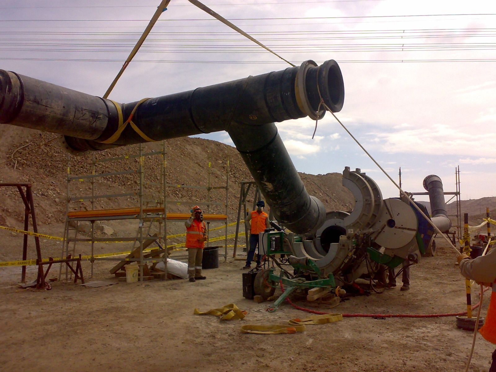 Instalación de una tubería industrial de gran tamaño en una obra de construcción, con trabajadores y andamios al atardecer.