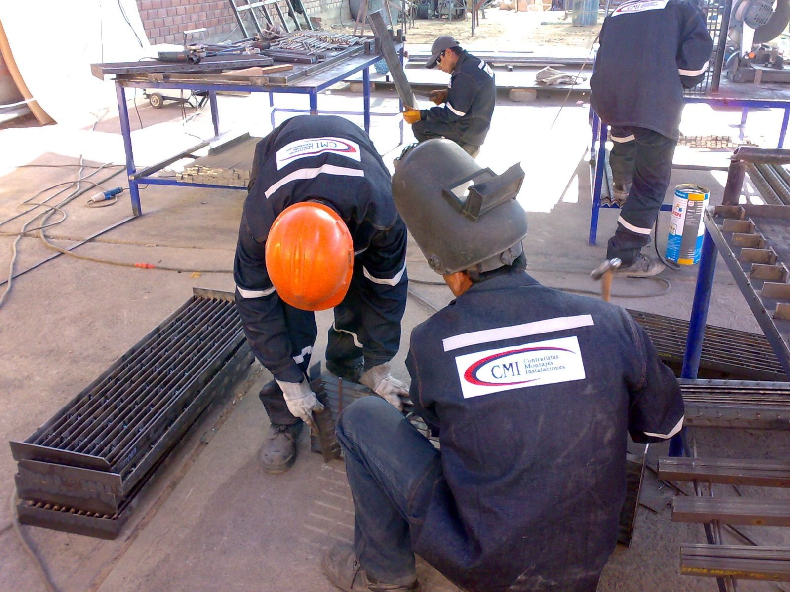 Trabajadores con cascos de seguridad se inclinan sobre una rejilla metálica en una obra de construcción al aire libre.