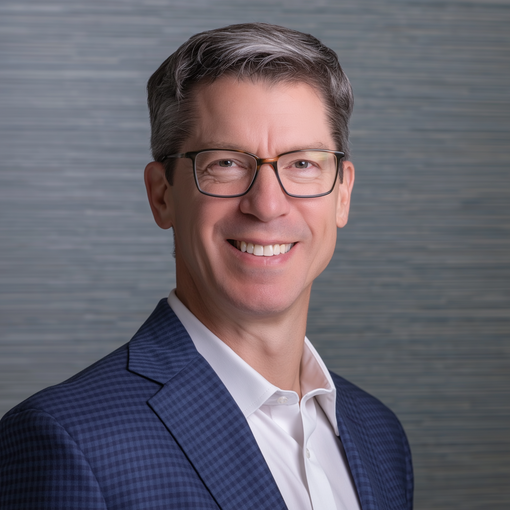 Man in a blue blazer and glasses, smiling, set against a textured, light blue background.