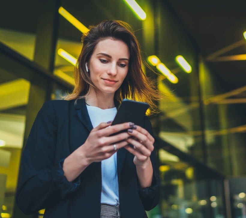 A woman in a black jacket is looking at her cell phone.