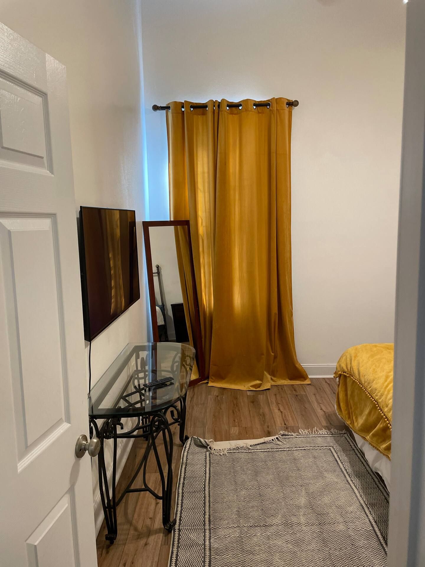 Bedroom with mustard curtains, a mirror, a rug, and a console table with a tv.