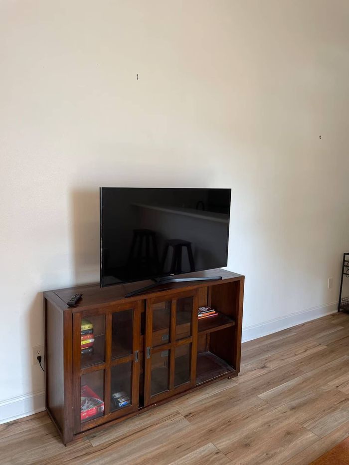 TV on a wooden cabinet against a plain wall and wood-look floor.
