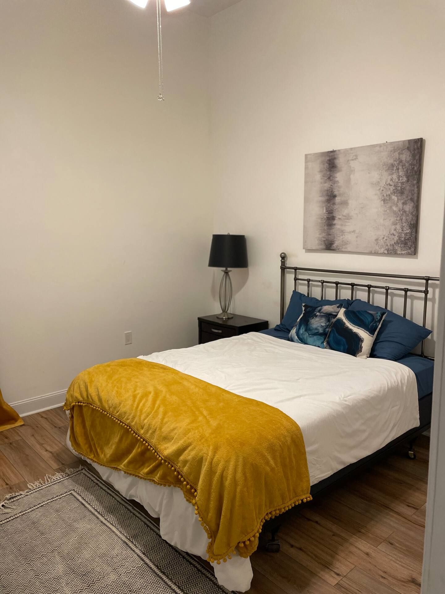 Bedroom with bed, nightstand, lamp, artwork, and yellow blanket.
