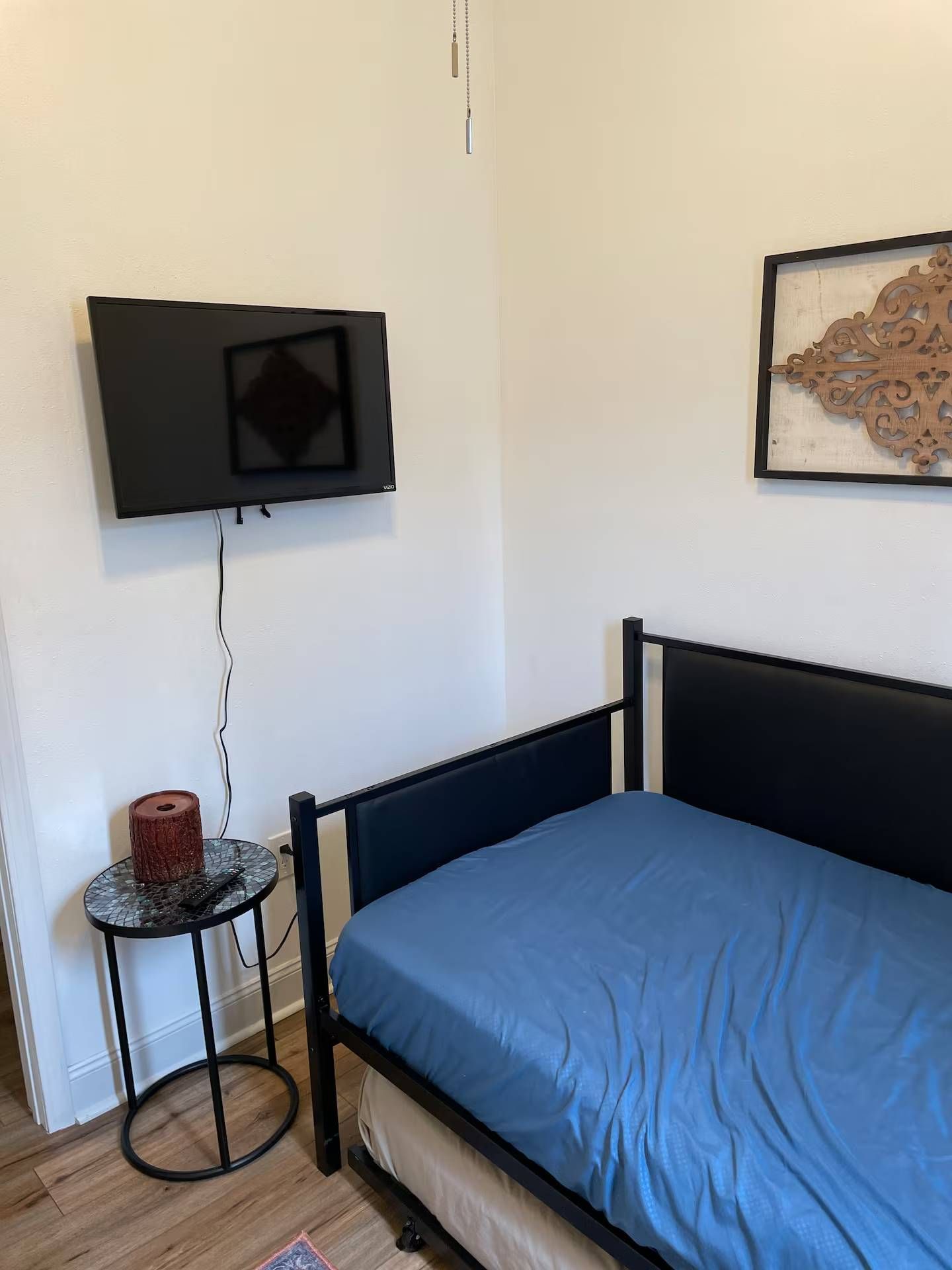 Bedroom with a bed, a TV mounted on the wall, and a side table with a lamp.