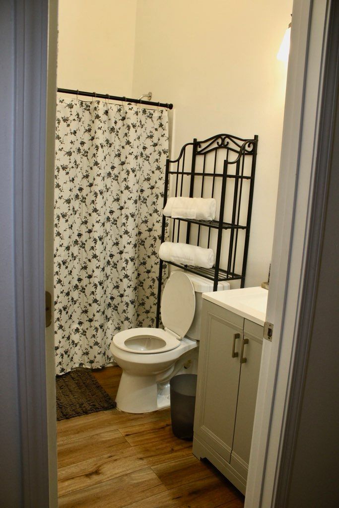 Bathroom with floral shower curtain, toilet, shelf with towels, and vanity.