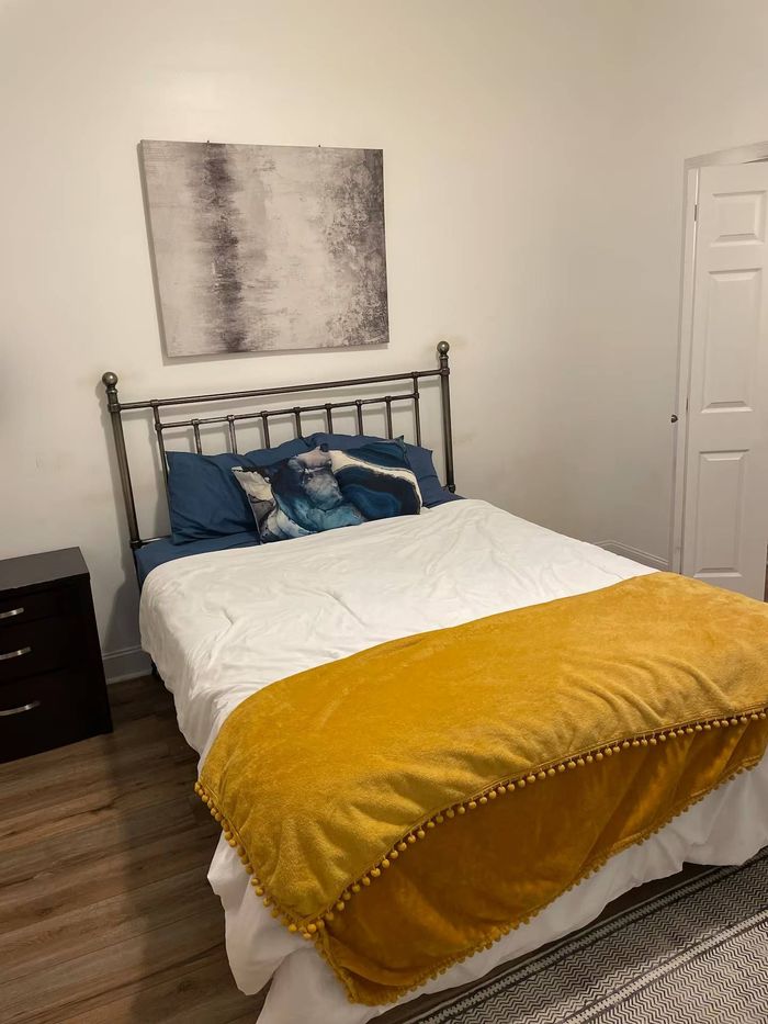 Bedroom with bed, nightstand, art, and mustard yellow blanket.