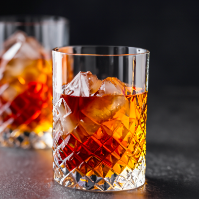 Two glasses of whiskey with ice in them on a table.