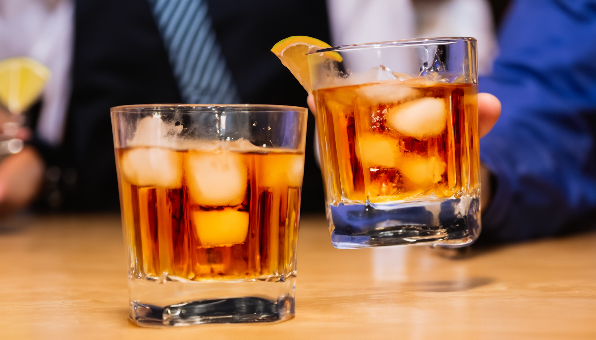 Two glasses of whiskey with ice and a lemon slice on a table.