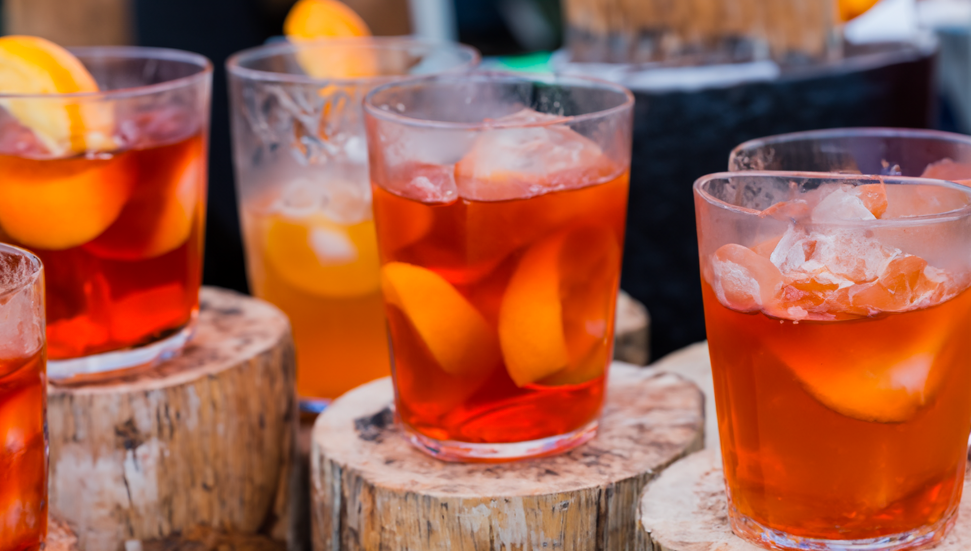 A group of glasses filled with orange juice and ice are sitting on wooden stump.