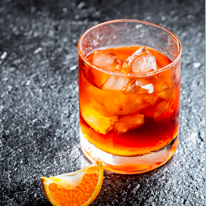 A glass of orange juice with ice and an orange slice on a table.
