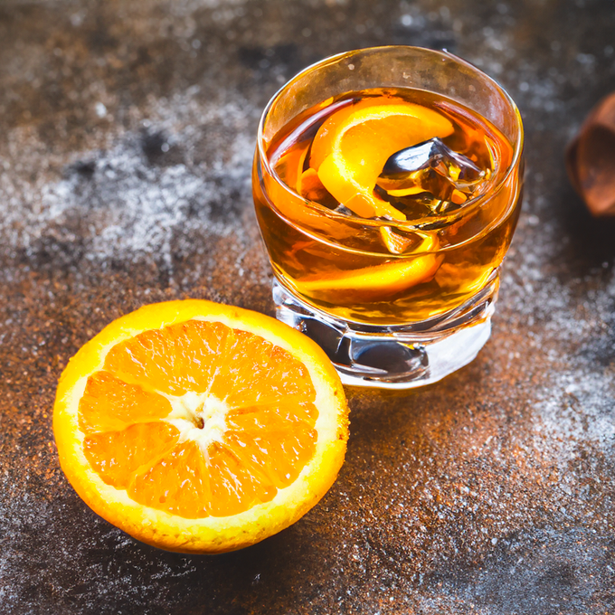 A glass of whiskey next to a slice of orange