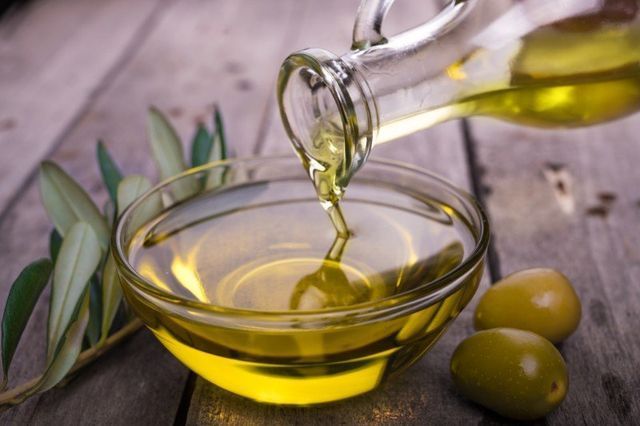 L'olio d'oliva viene versato in una ciotola di vetro su un tavolo di legno.
