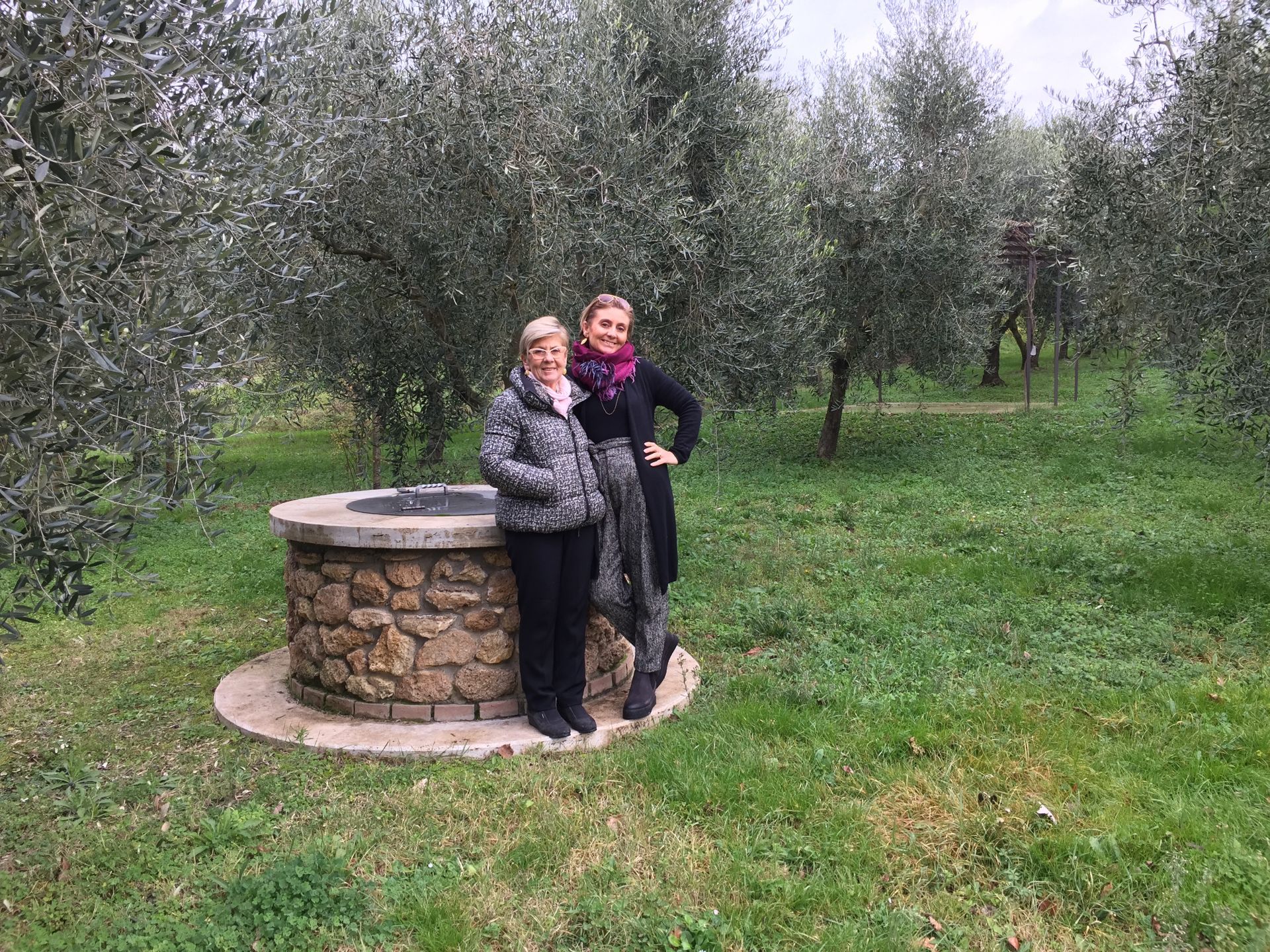 Due donne sono in piedi accanto a un pozzo di pietra in un campo.