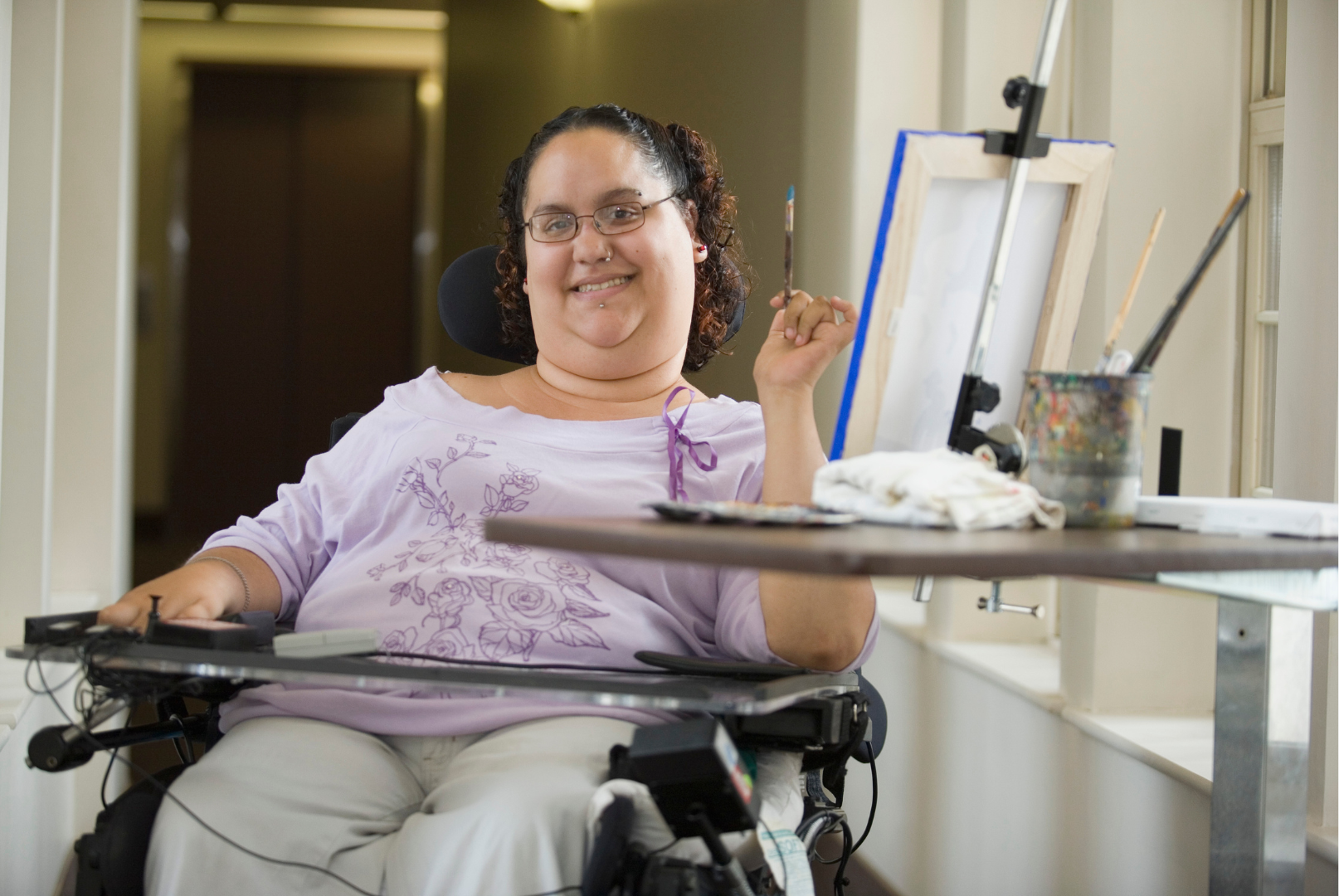 a woman in a wheelchair is sitting at a table with a painting on it .