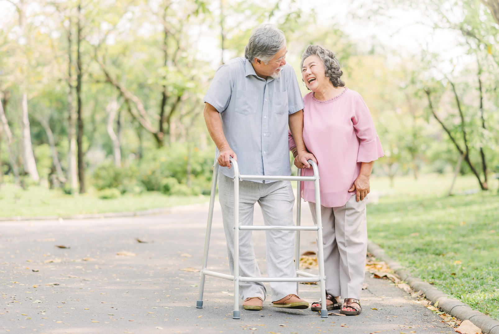 an elderly couple is walking in the park with a walker .