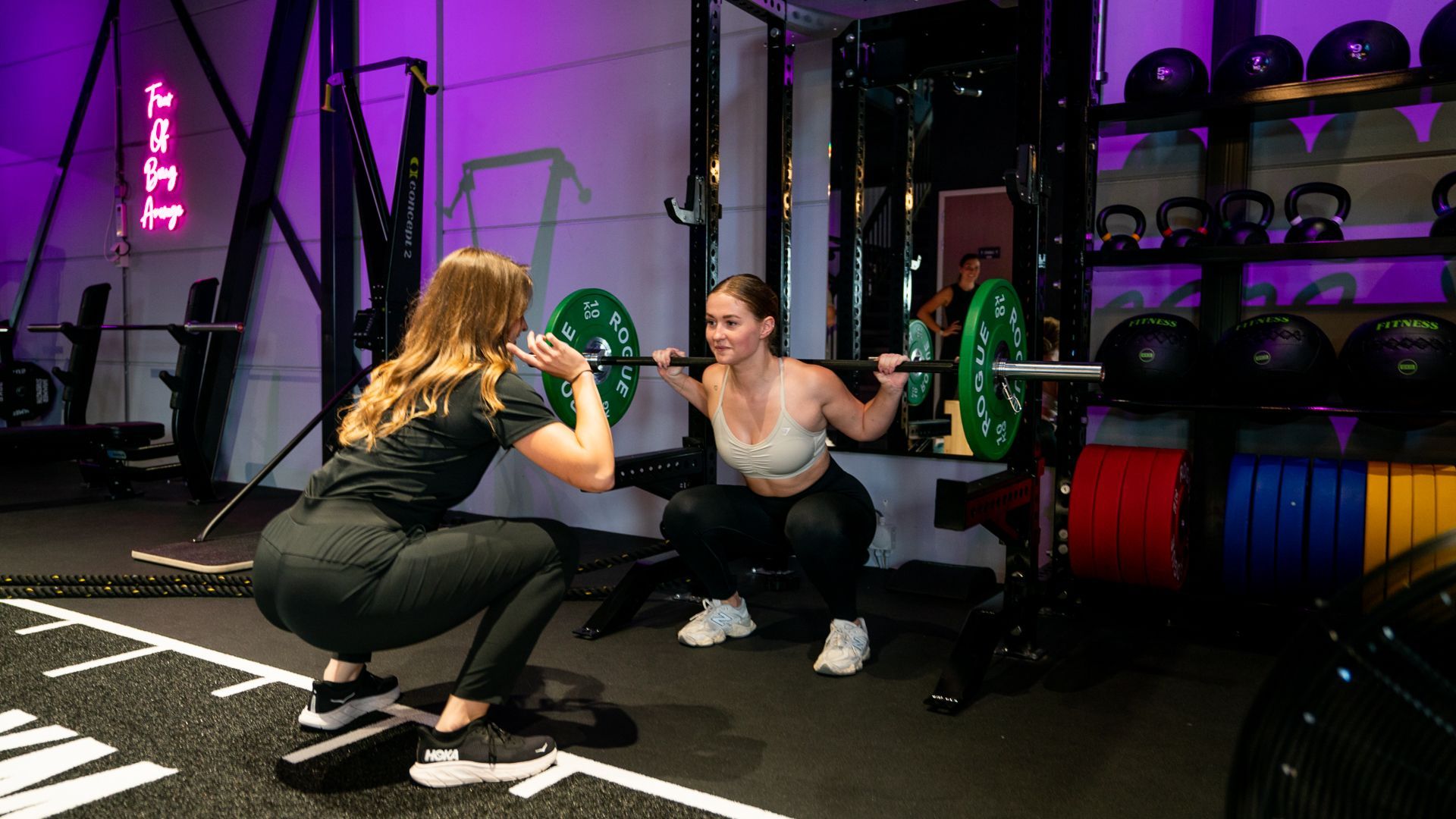 Twee vrouwen hurken met een halter in een sportschool.