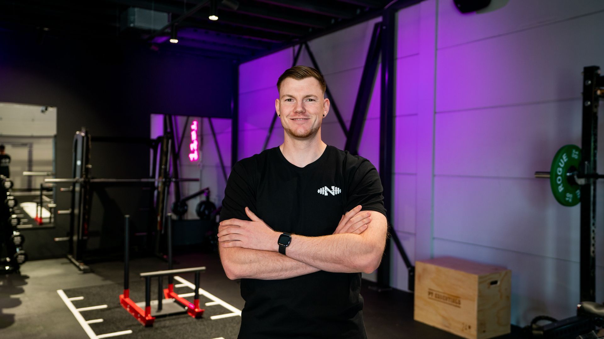 Een man staat in een sportschool met zijn armen over elkaar.