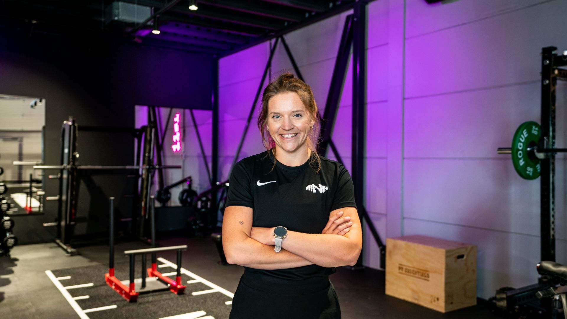 Een vrouw staat in een sportschool met haar armen over elkaar.