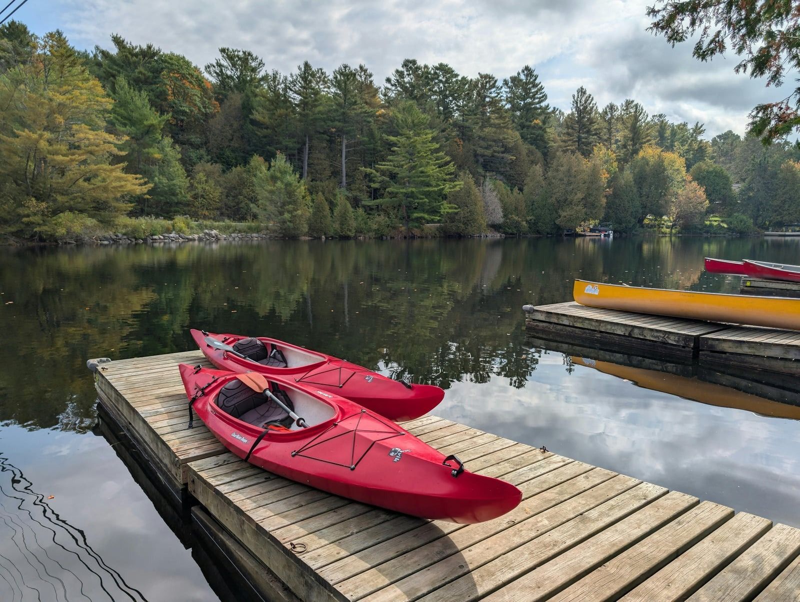 Two red kayaks on a wooden dock by a calm lake with trees reflected in the water