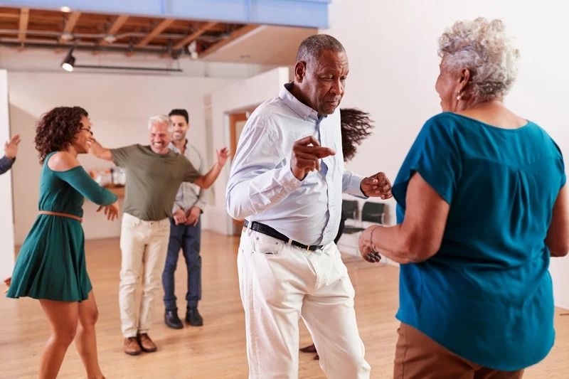 People dancing in a bright studio, with two couples in casual clothes facing each other.