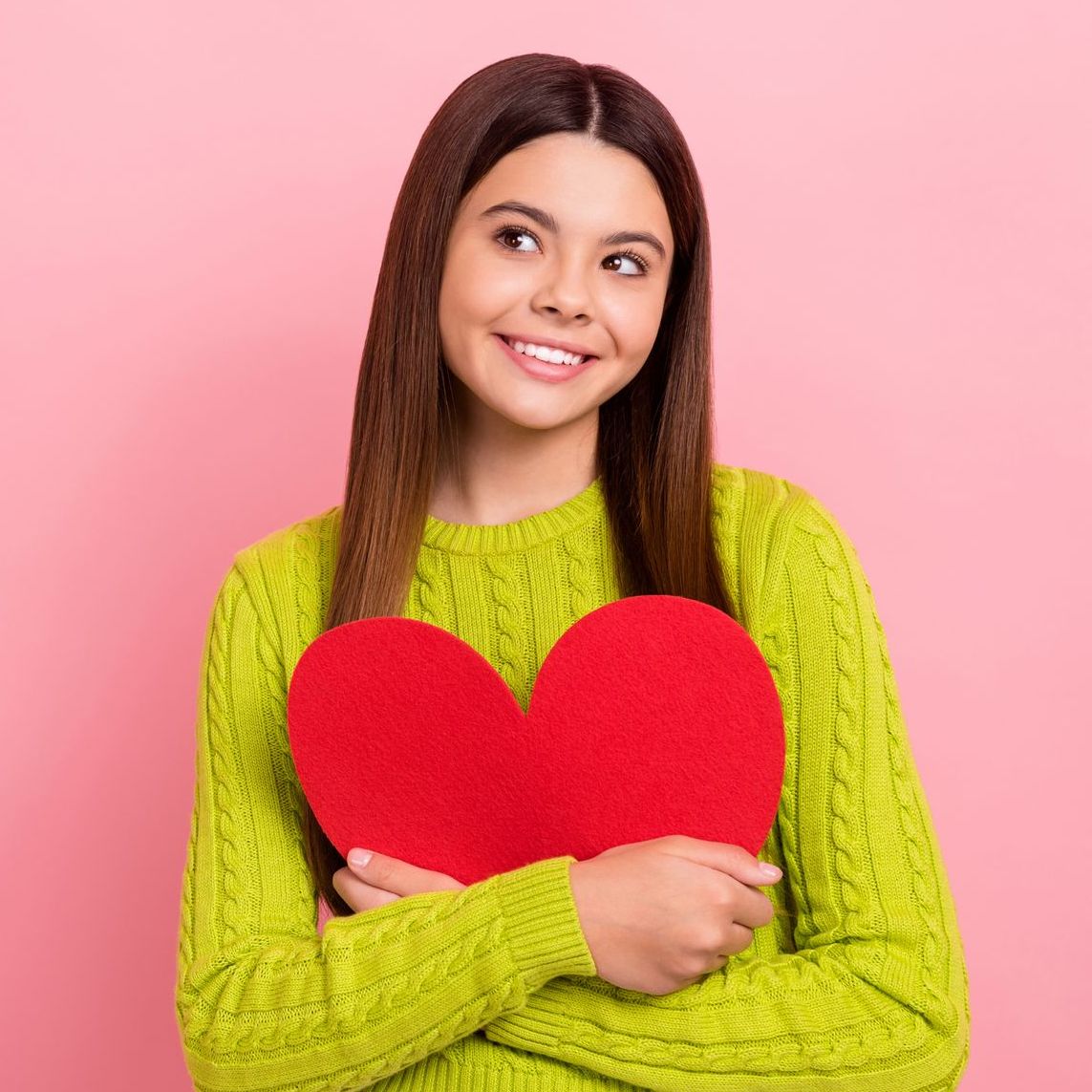 A woman in a green sweater is holding a red heart.