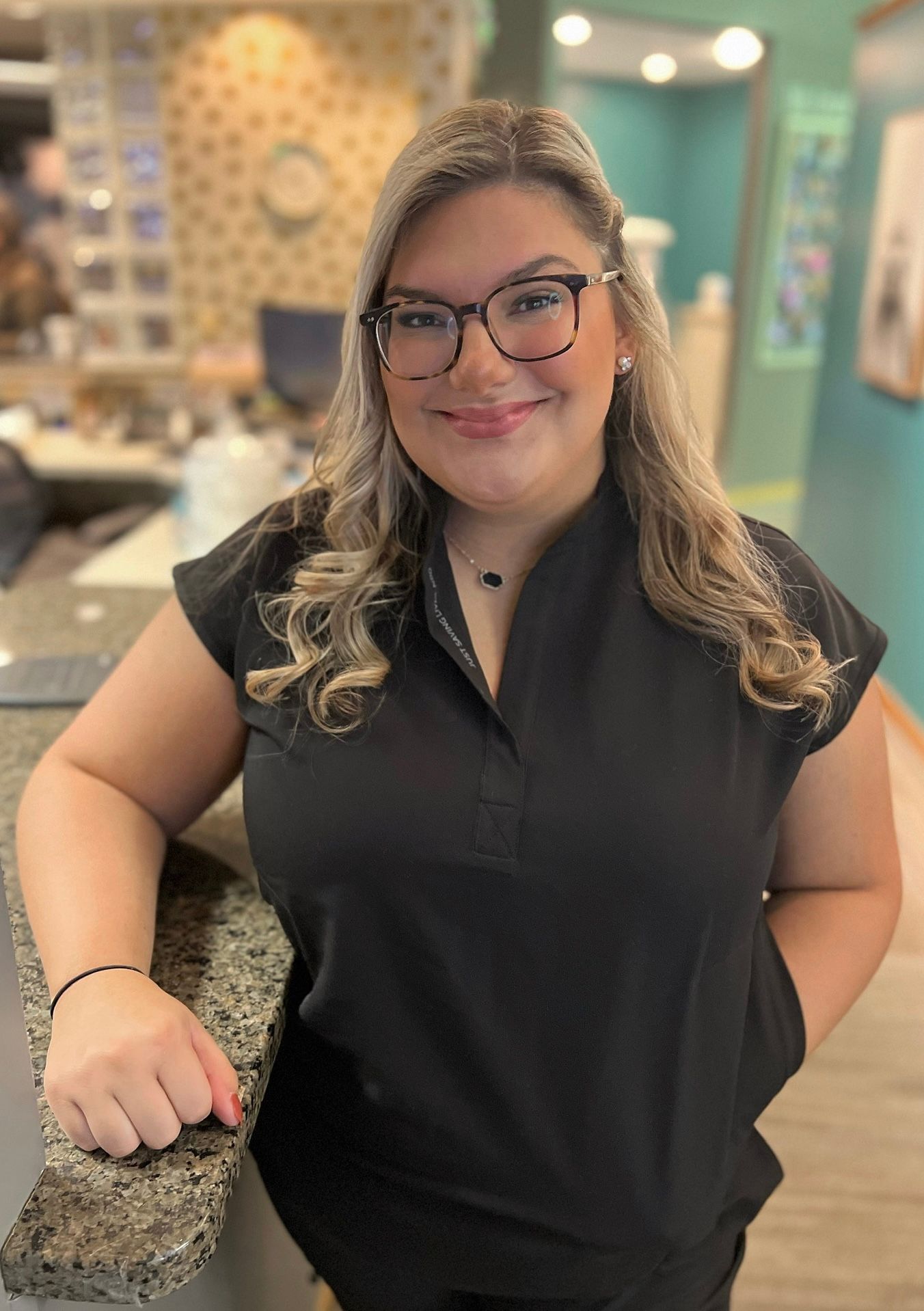 A woman wearing glasses and a black shirt is standing in front of a counter.