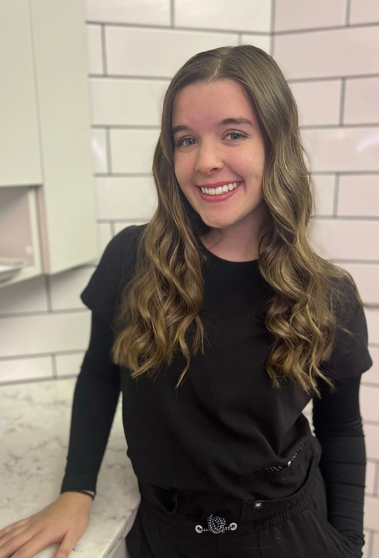 A woman in a black shirt is standing next to a counter and smiling.