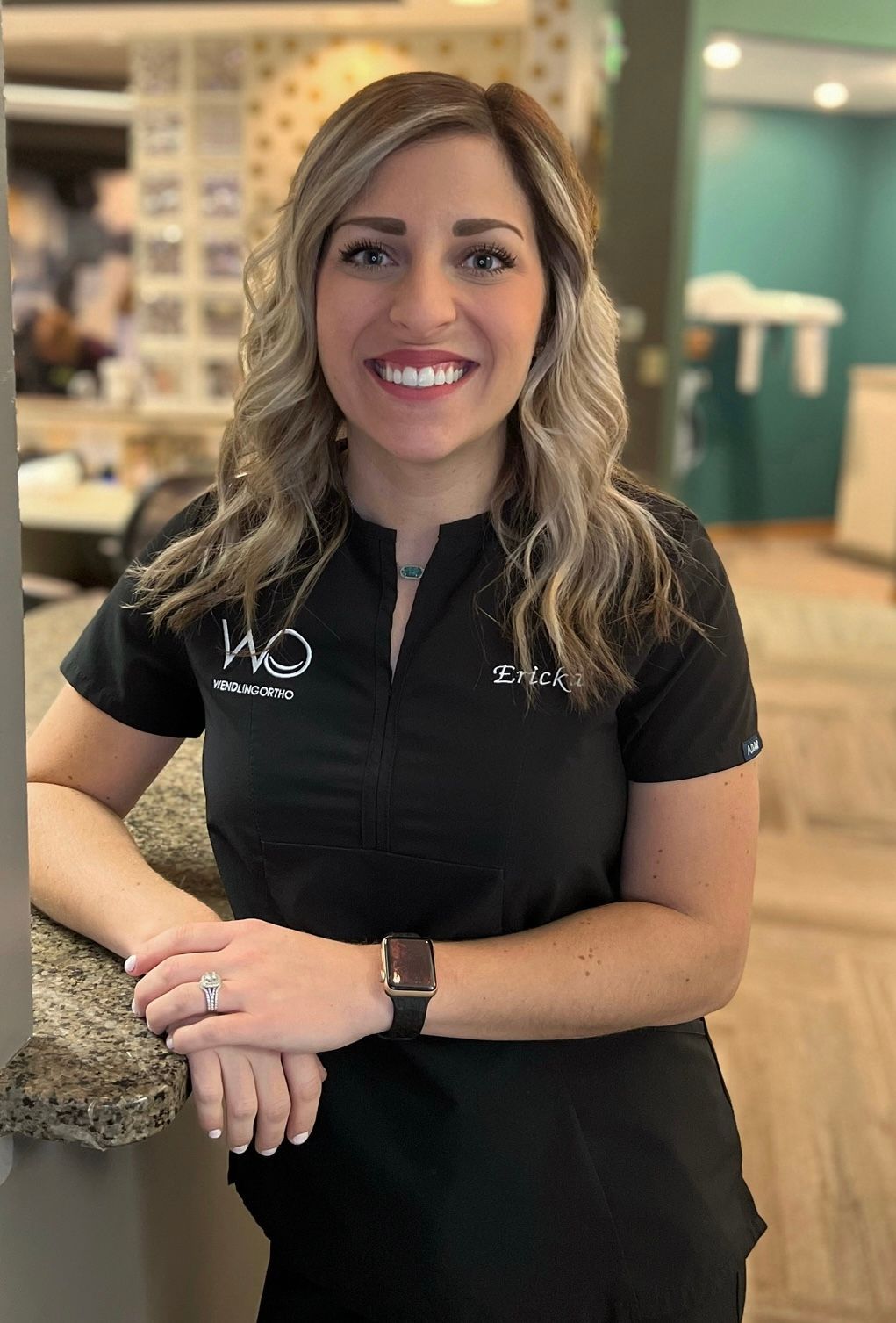 A woman in a black shirt is standing next to a counter and smiling.
