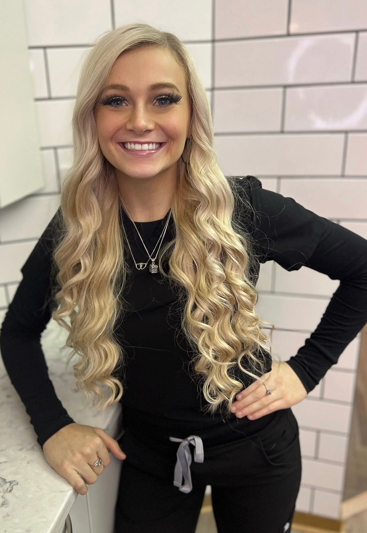 A woman with long blonde hair is standing in a kitchen with her hands on her hips.