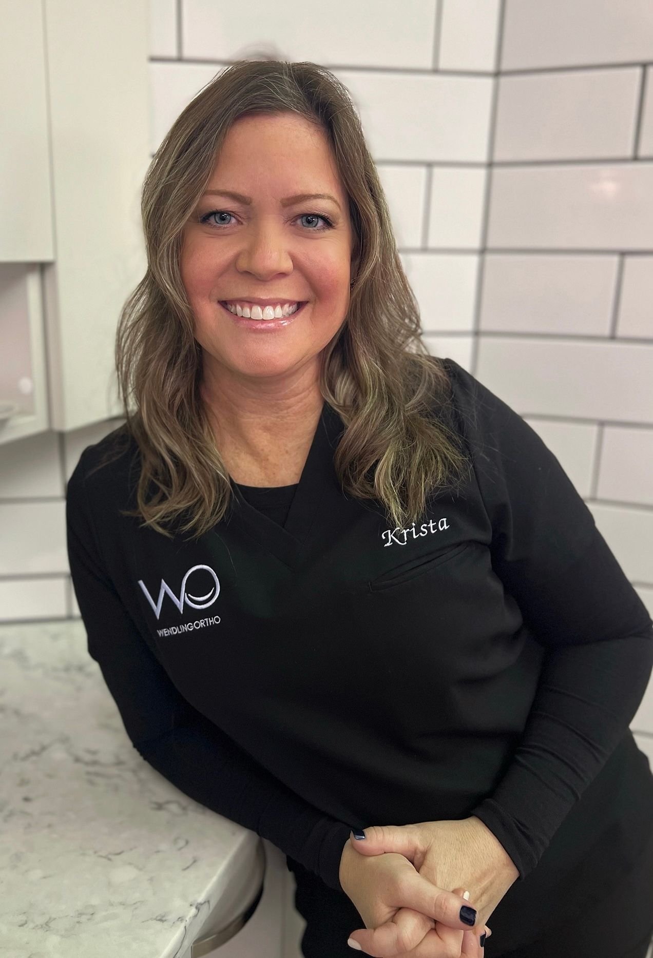 A woman in a black shirt is standing next to a counter and smiling.