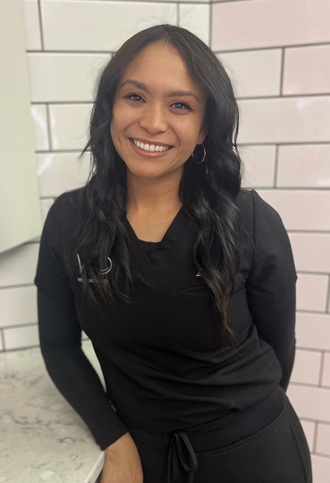 A woman in a black shirt is standing next to a counter and smiling.