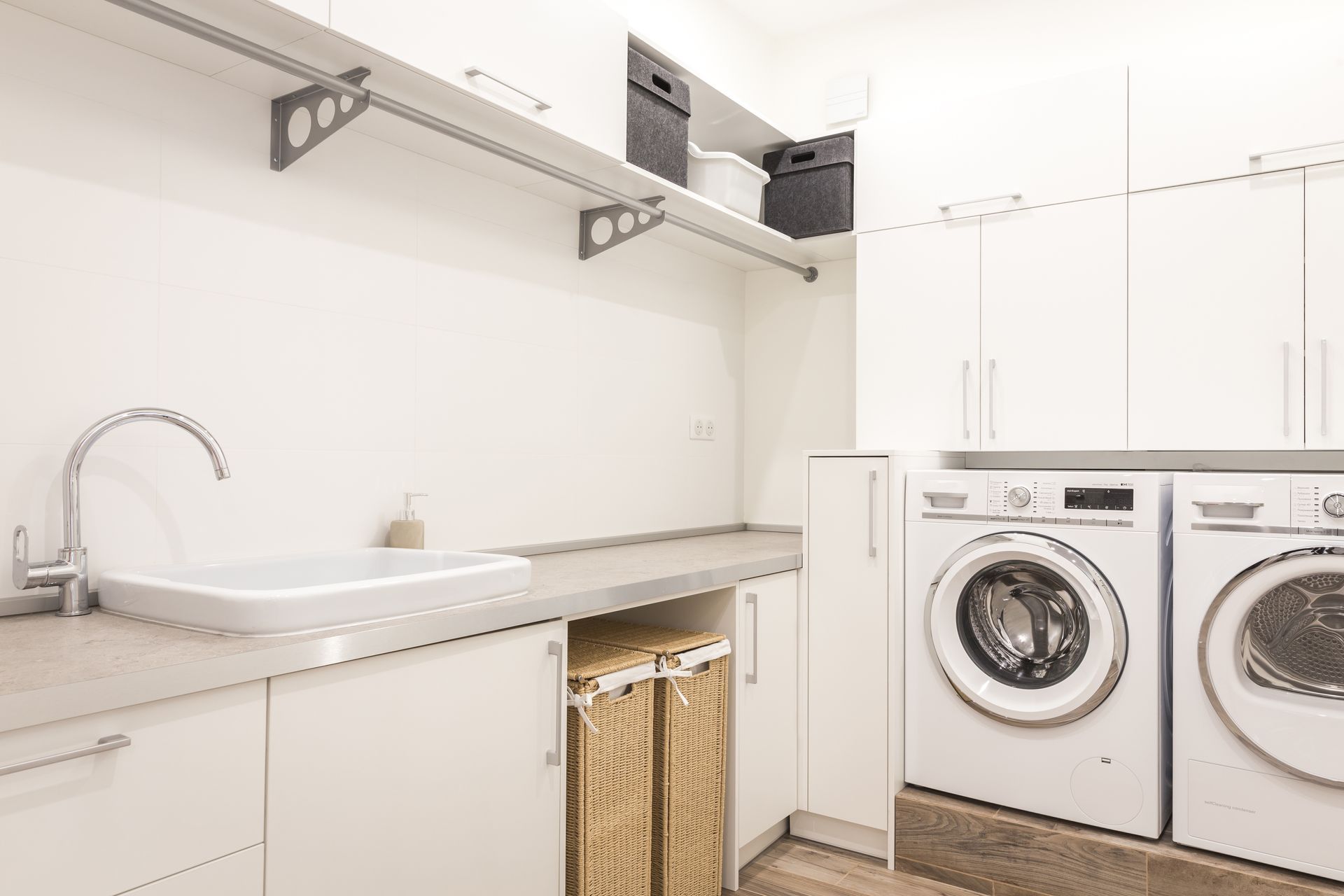 White laundry room with washing machine, sink, cabinets, shelves, and baskets.