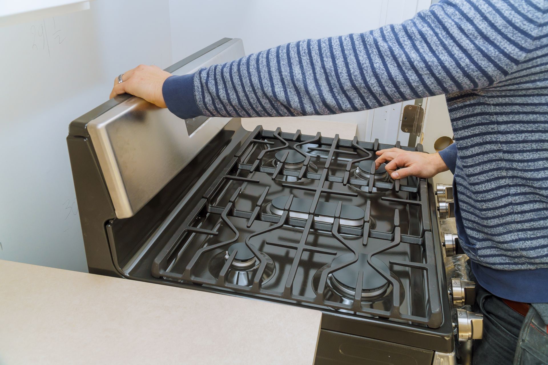 Person lifts the metal cover of a gas stovetop in a kitchen.