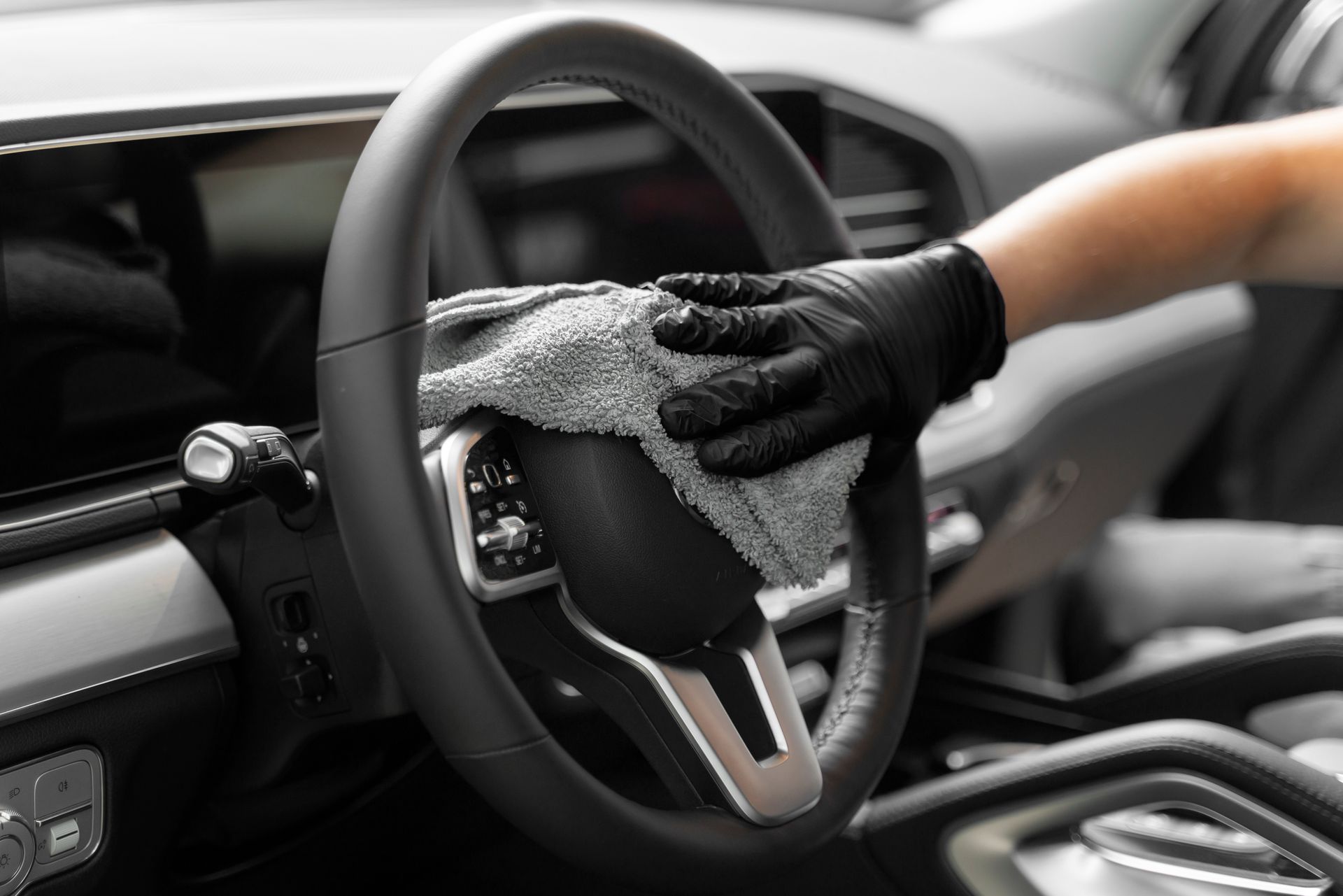 A person is cleaning the steering wheel of a car with a cloth.