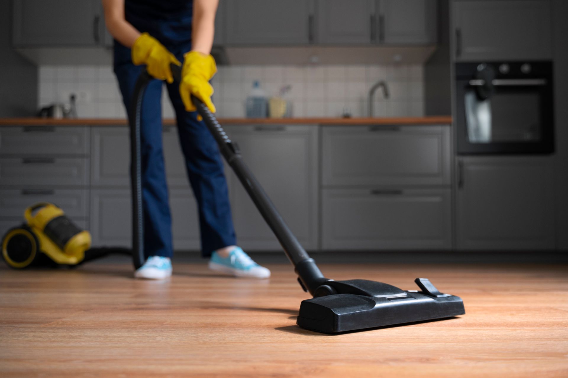 A woman is using a vacuum cleaner to clean the floor in a kitchen.