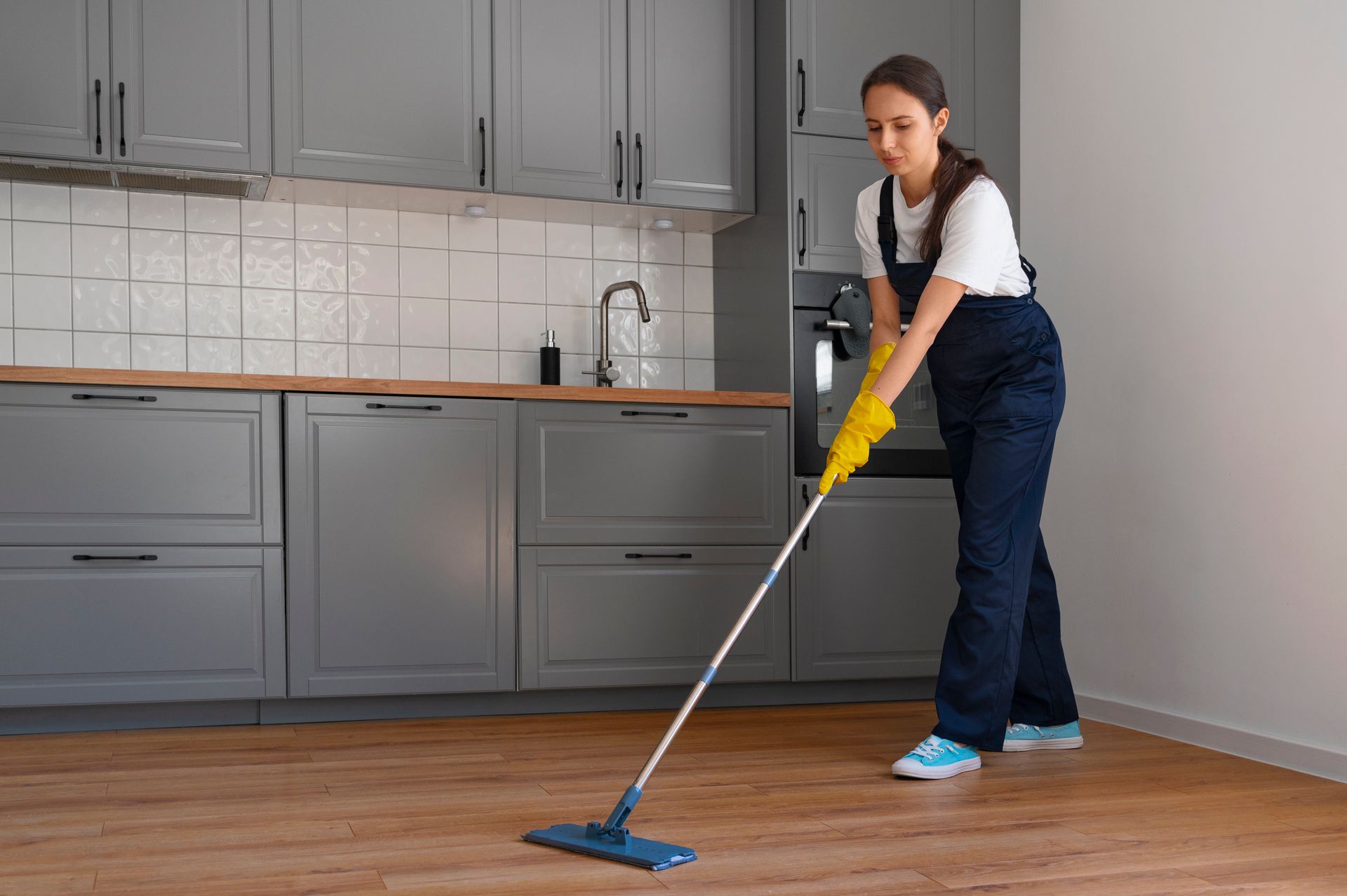 A woman is cleaning the floor in a kitchen with a mop.