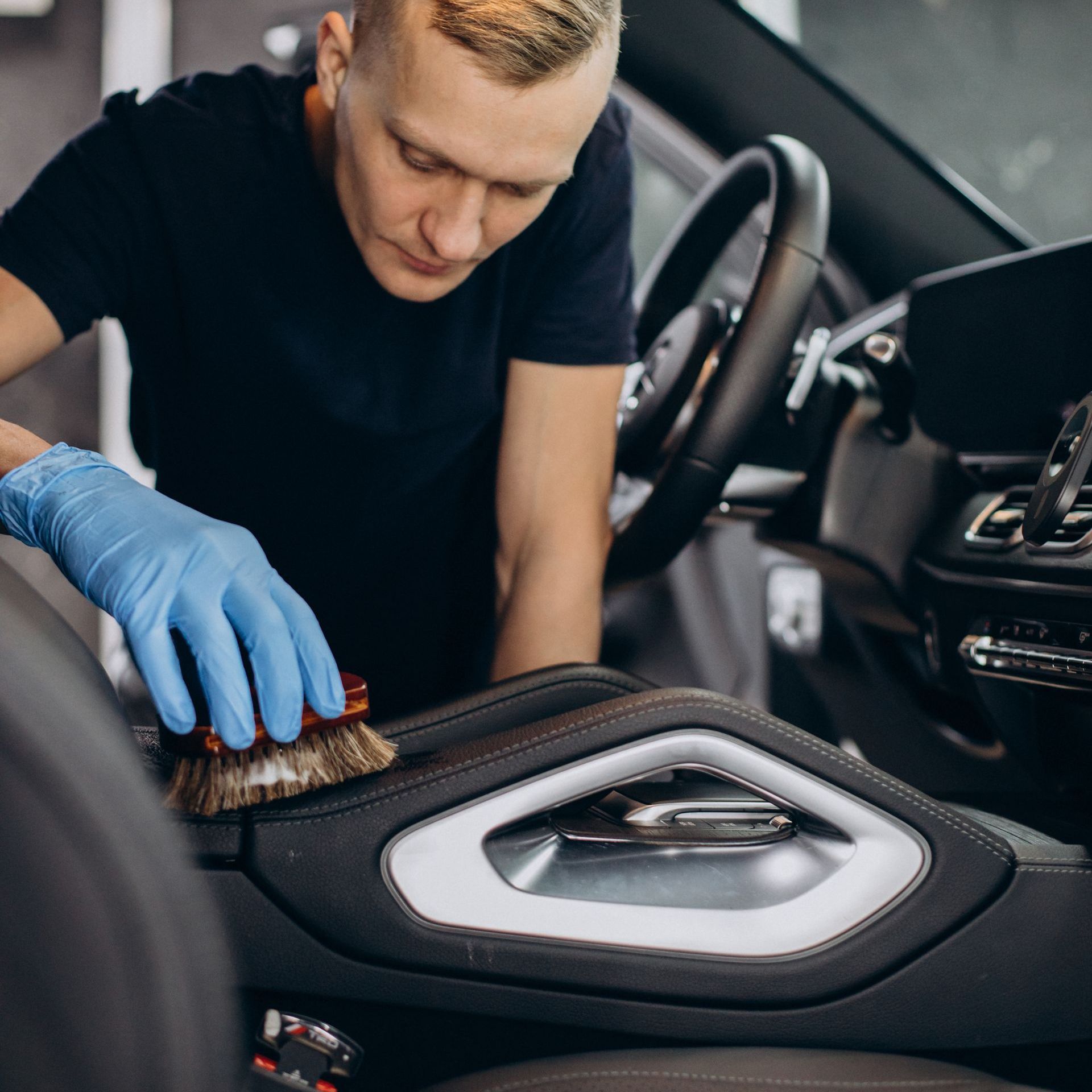 A man wearing blue gloves is cleaning a car seat with a brush.