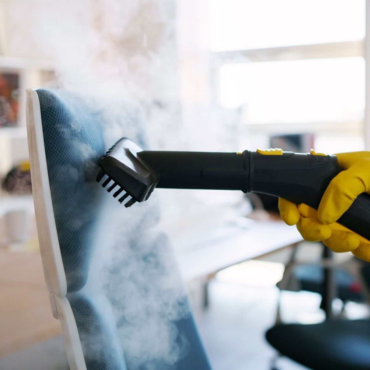 A person wearing yellow gloves is using a steam cleaner to clean a chair