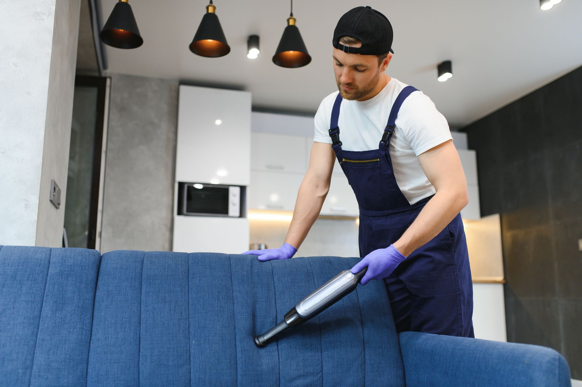 A man is cleaning a blue couch with a vacuum cleaner.