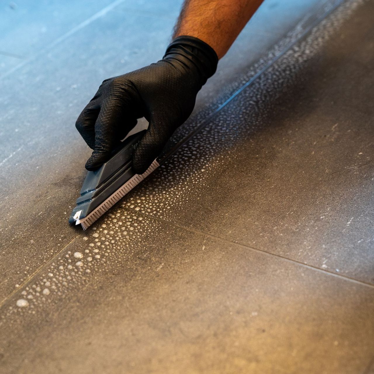 A person wearing black gloves is cleaning a tile floor with a brush
