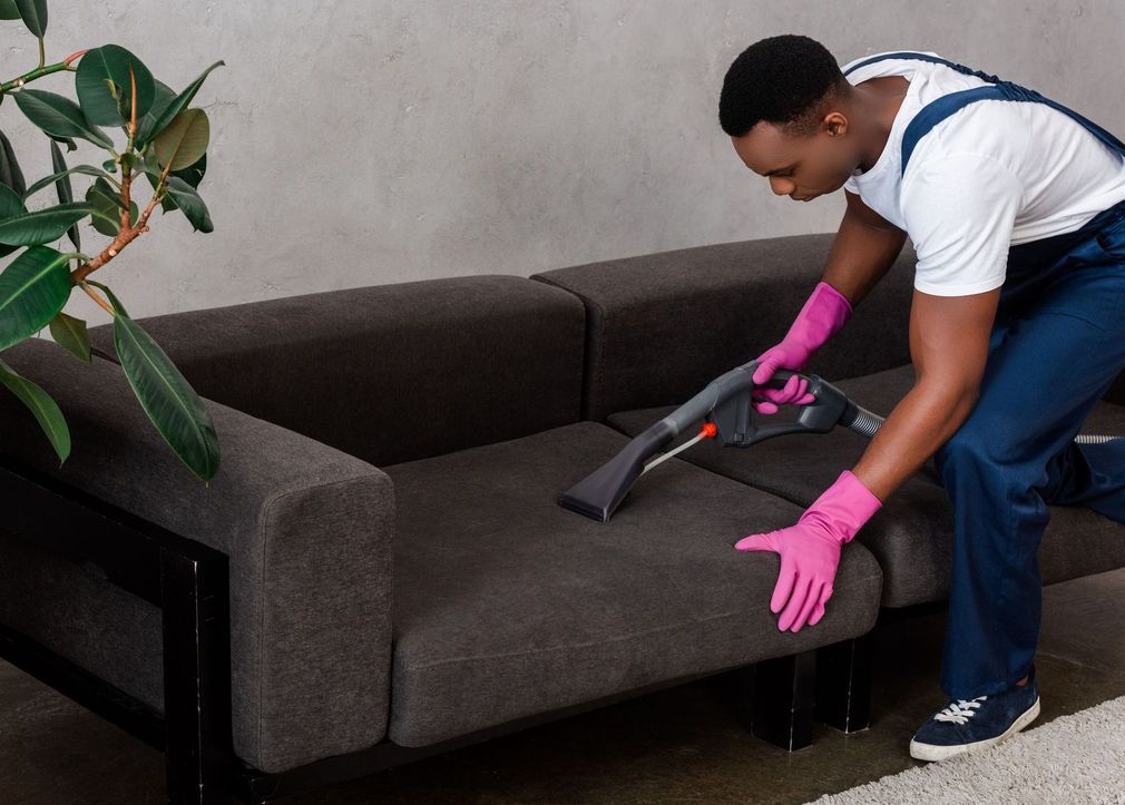 A man is cleaning a couch with a vacuum cleaner.