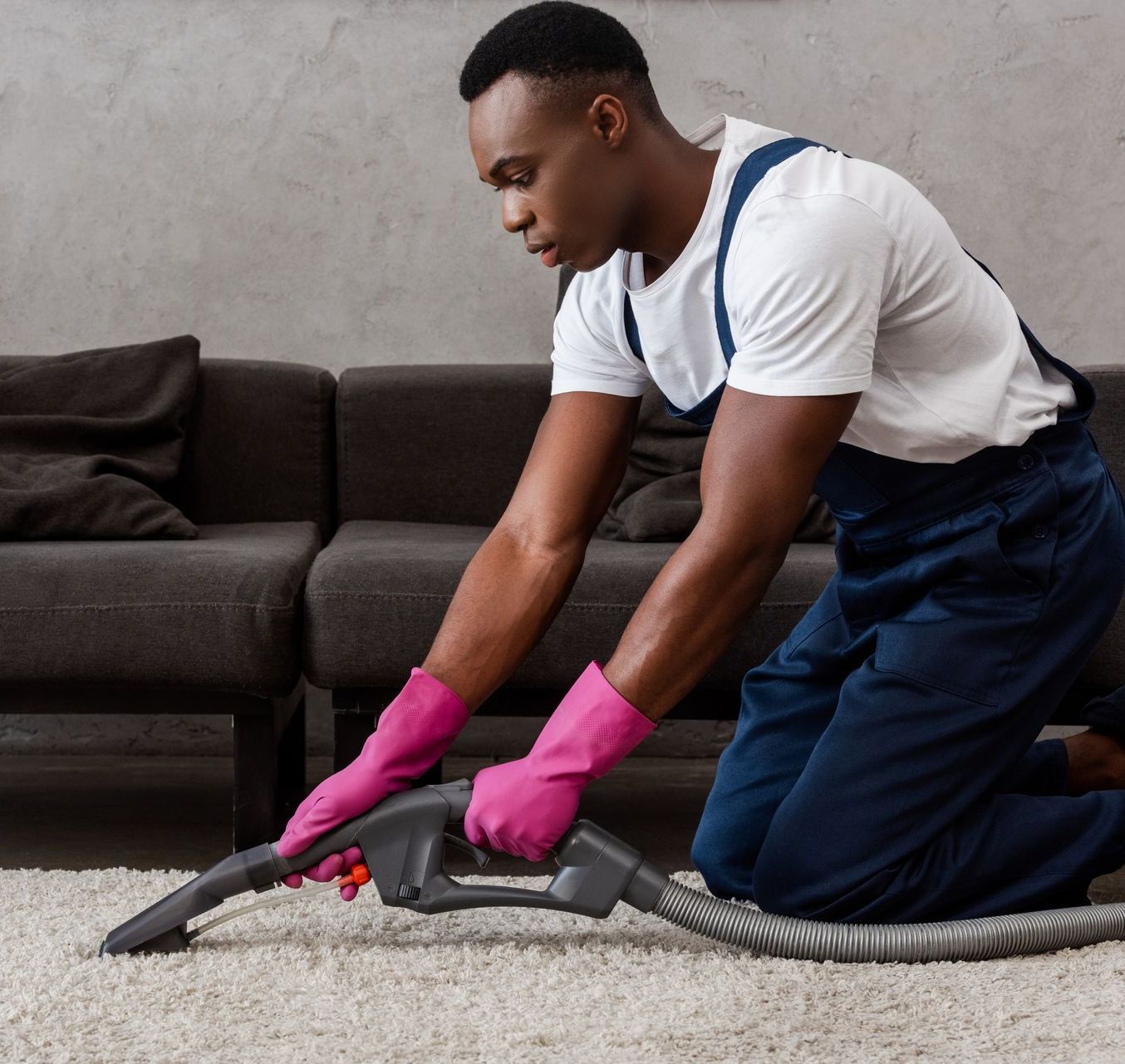A man wearing pink gloves is cleaning a carpet with a vacuum cleaner.