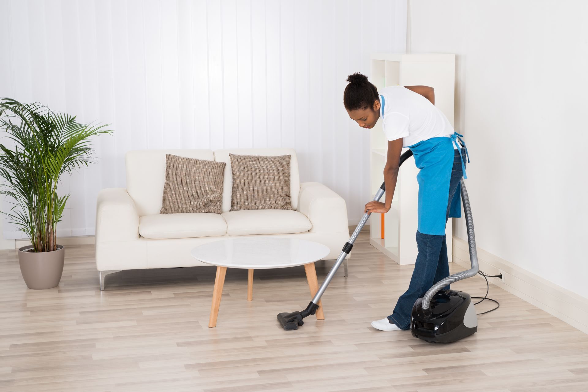 A woman is cleaning the floor with a vacuum cleaner in a living room.